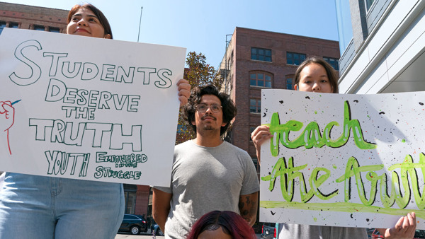 Three students hold protest signs saying "Students Deserve the Truth" and "Teach the Truth"