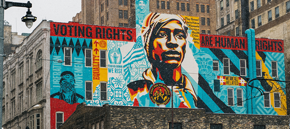 A mural painted on a building says "Voting Rights are Human Rights" with faces of people of color.