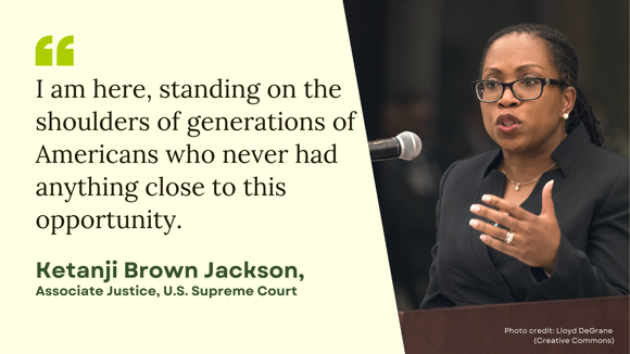 Associate Justice Ketanji Brown Jackson stands at a podium during a speaking event. Her quote is written beside her, "I am here, standing on the shoulders of generations of Americans who never had anything close to this opportunity."