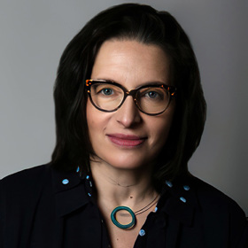 Ellen Buchman sits for a headshot wearing glasses and a black blazer.