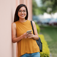 A student holding her phone, leaning against a wall and smiling