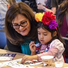 A child with a flower crown makes art next to a parent