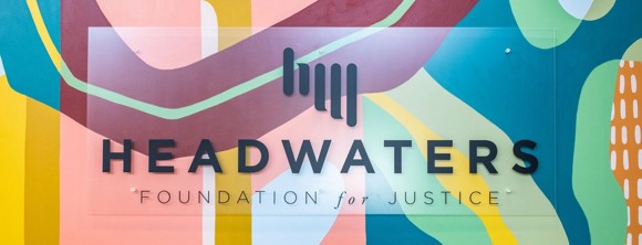 A photo of the Headwaters sign in front of a mural in our office