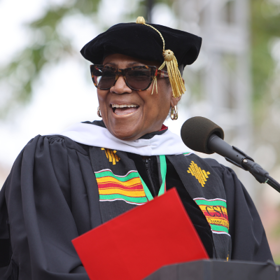 Angela Timmons smiling at the microphone stand wearing doctoral regalia