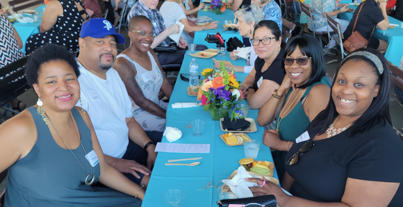 People smiling up at the camera, blue table cloths, flowers, and snacks on the table