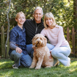 Meryl and Jonathan Chase posing with their son Kyler and their labradoodle Teddi Bear in a backyard for a family photo