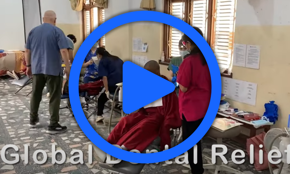 A video thumbnail with an image of a Tibetan temple with dentist chairs set up. Volunteers stand in front of students in red robes sitting on the chairs